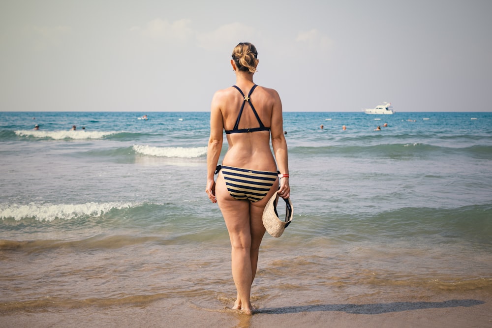woman holding sunvisor cap wearing striped bikini
