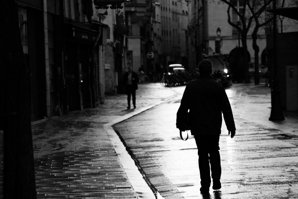 grayscale photography of woman walking beside building