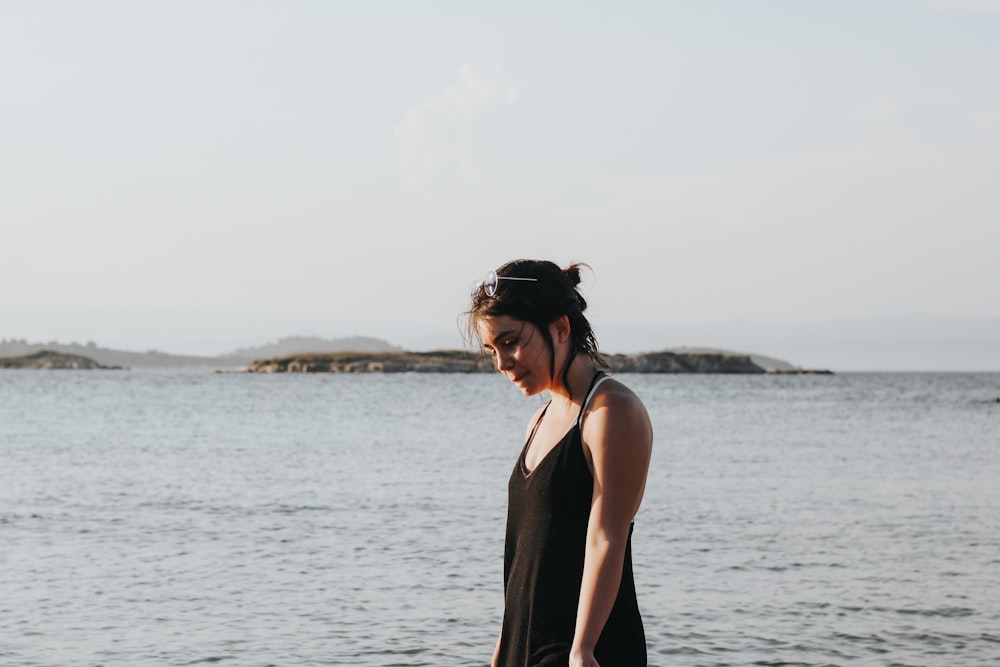 donna che indossa abito nero con spalline sottili accanto alla spiaggia