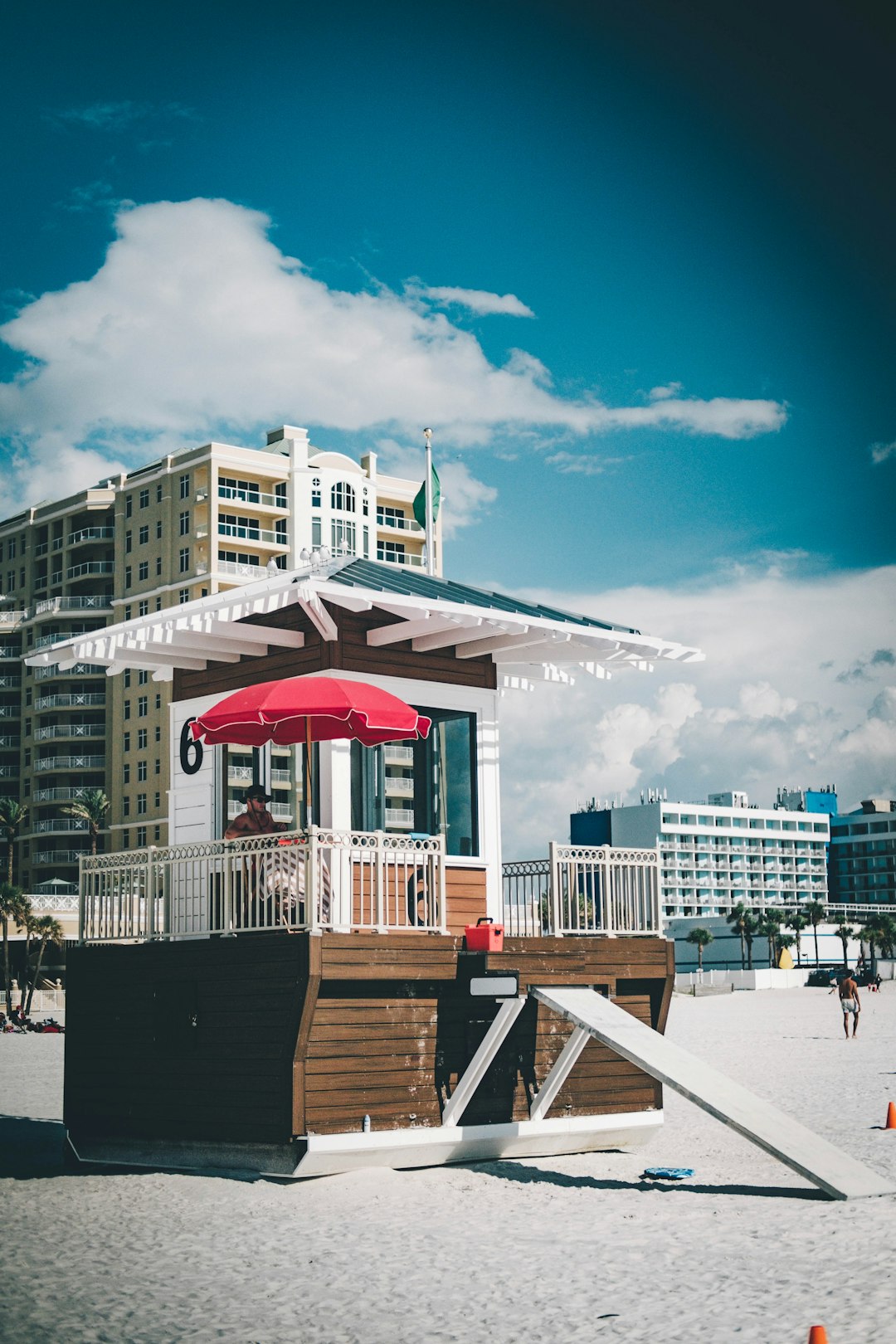 brown and white wooden lifeguard house on beach near hotel and buildings under blue and white skies during daytime