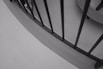 A monochrome photograph featuring a curved iron railing with vertical bars, set against a smooth concrete surface. The straight lines of the rails create a stark contrast with the curved background. The composition focuses on geometric shapes and patterns, enhancing the structural elegance of the scene.
