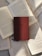 A hardcover book with a maroon cover rests on top of several open books with visible text. The pages of the open books are arranged in a slightly scattered pattern, creating a layered effect. Sunlight casts soft shadows across the books, highlighting the textures of the paper and the cover.