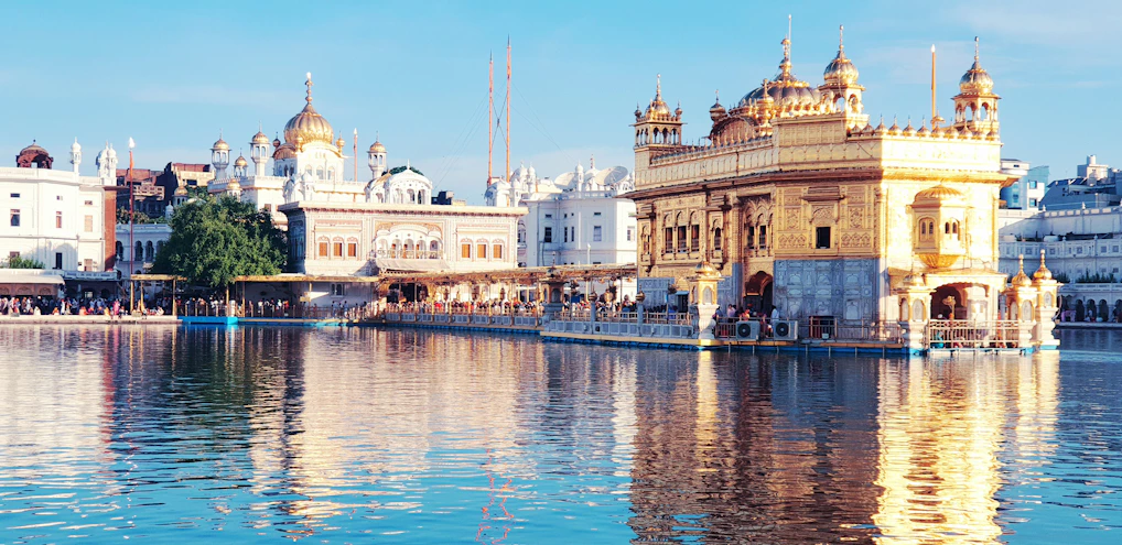 A serene temple courtyard bathed in soft morning light, with saffron decorations and worshippers in peaceful prayer.