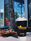A stylish reusable coffee cup with Quimbayan Coffee branding on a city street bench.
