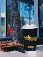 A stylish reusable coffee cup with Quimbayan Coffee branding on a city street bench.