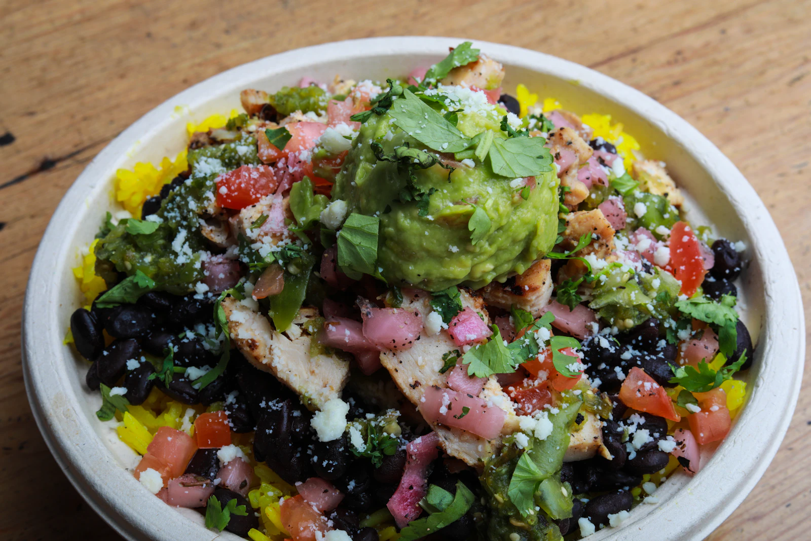 Loaded rice bowl with black beans, grilled chicken, guacamole, pico de gallo, and cotija cheese
