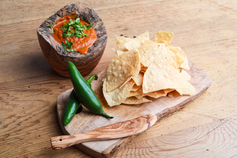 Roasted red salsa in a wooden mortar beside two jalapenos and a pile of tortilla chips