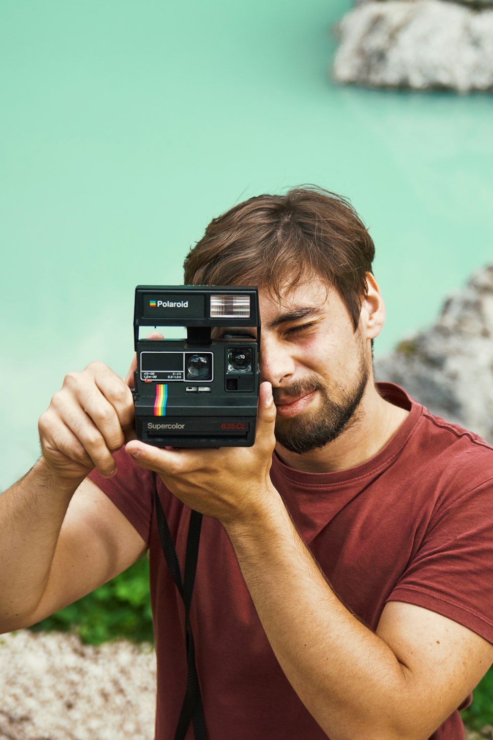 hombre con camisa granate de cuello redondo sosteniendo una cámara Polaroid instantánea negra