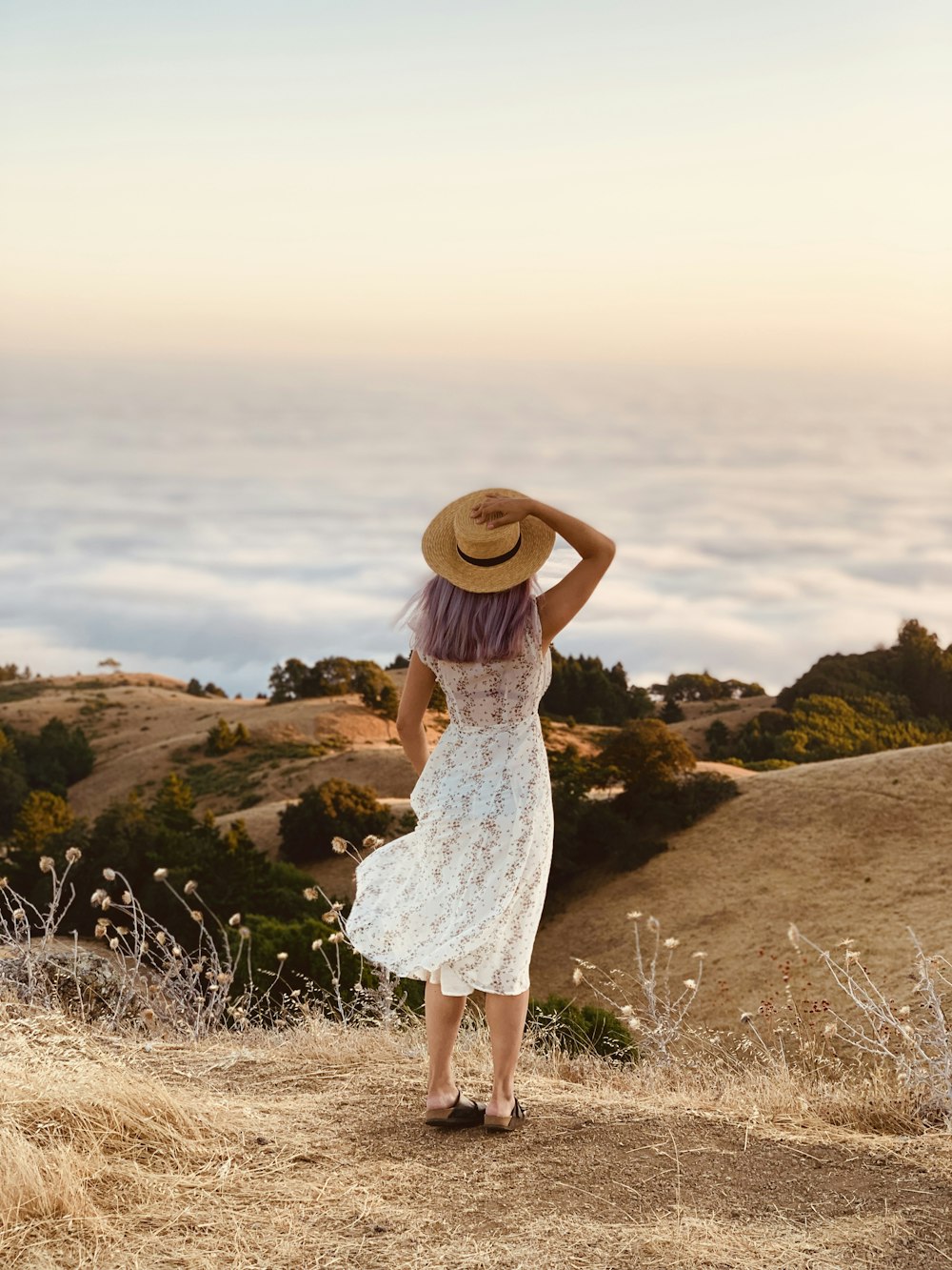 Vestido de encaje blanco para mujer y sombrero marrón para el sol en la cima de la colina durante el día