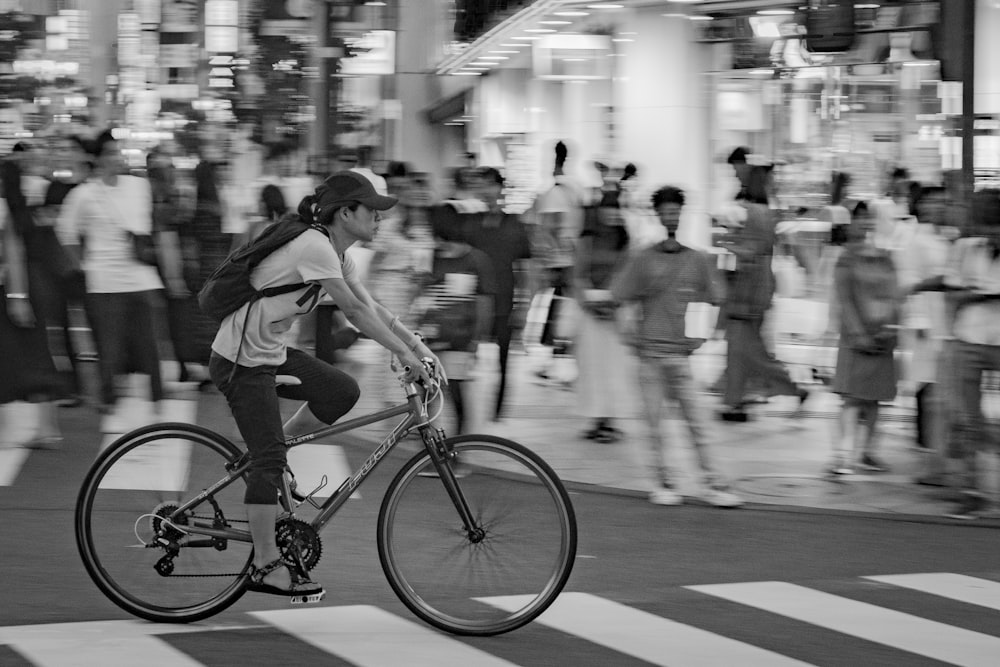 grayscale photo of man riding bike crossing pedestrian