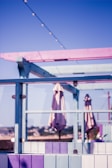 A vibrant outdoor terrace with a pastel color scheme featuring shades of pink, purple, and blue. The area includes umbrellas, glass panels, and string lights overhead, suggesting a relaxed and inviting atmosphere with a view of a distant landscape.