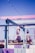 A vibrant outdoor terrace with a pastel color scheme featuring shades of pink, purple, and blue. The area includes umbrellas, glass panels, and string lights overhead, suggesting a relaxed and inviting atmosphere with a view of a distant landscape.