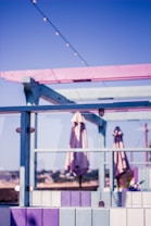 A vibrant outdoor terrace with a pastel color scheme featuring shades of pink, purple, and blue. The area includes umbrellas, glass panels, and string lights overhead, suggesting a relaxed and inviting atmosphere with a view of a distant landscape.