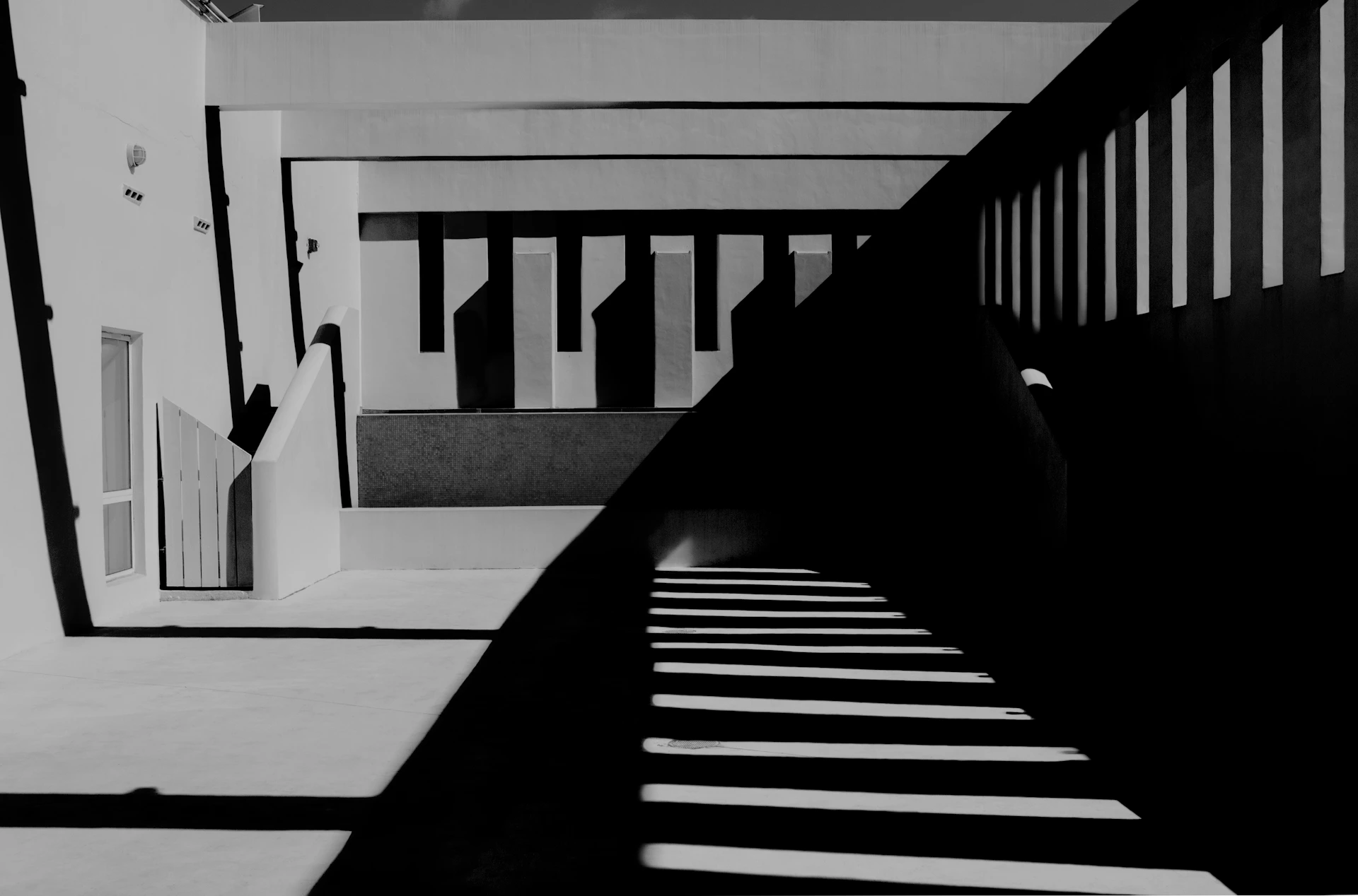 Minimalist urban scene in monochrome, capturing sharp contrasts between shadows and light on architectural lines.