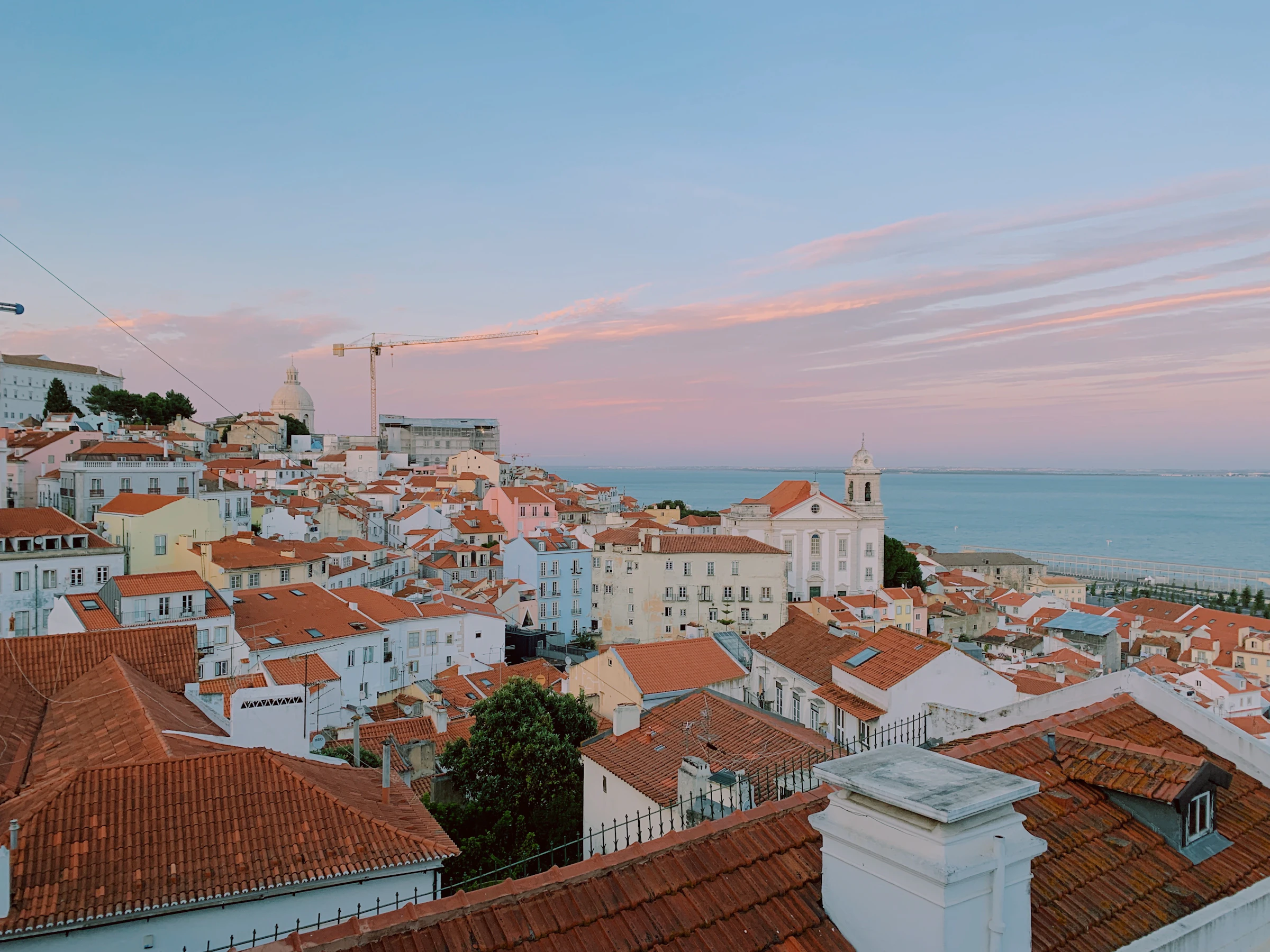 Daken van Alfama bij zonsondergang, gezien vanaf het Miradouro de Santa Luzia — met de Igreja de Santo Estêvão; op de achtergrond renovatiewerk bij het Panteão Nacional