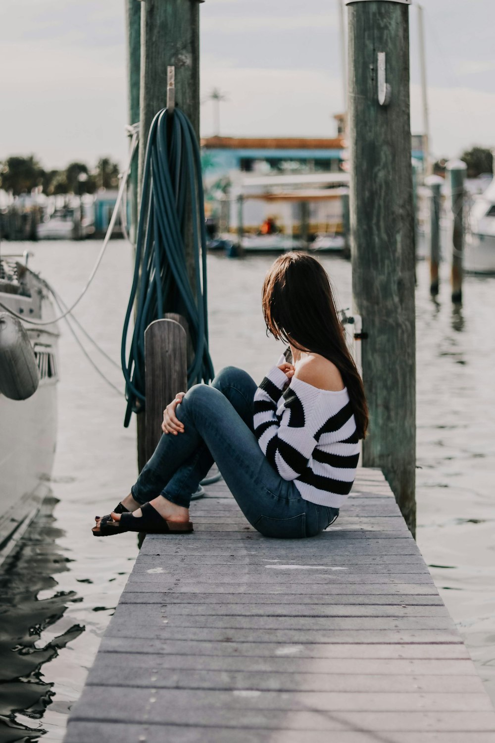woman in striped blouse and blue jeans sitting on wooden dock