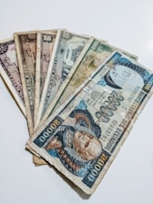 A collection of vintage currency notes fanned out on a flat surface. The notes display a variety of colors, designs, and denominations, suggesting they are from different historical periods or countries.