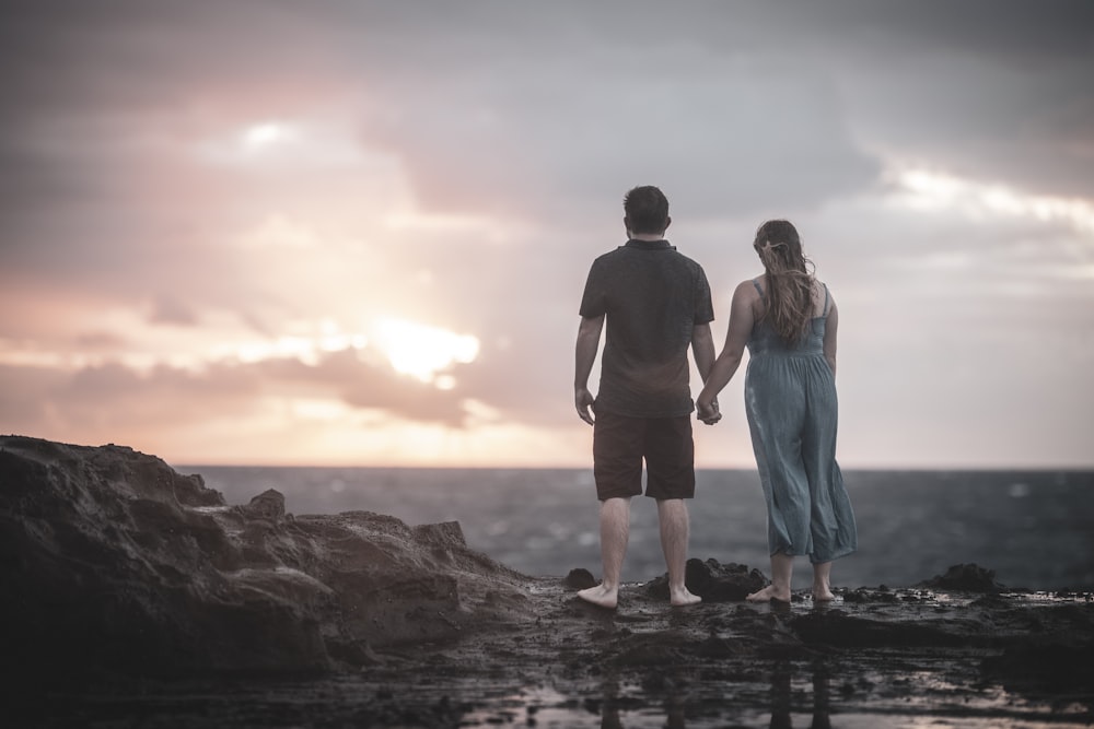 man and woman standing beside rock formation during golden hour