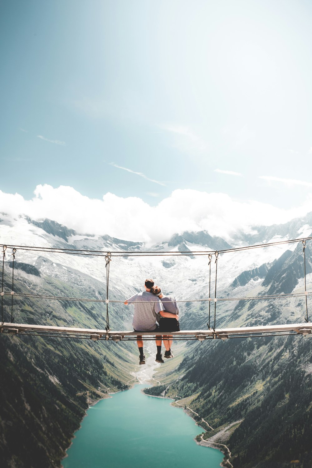 man and woman sitting on hanging bridge at daytime