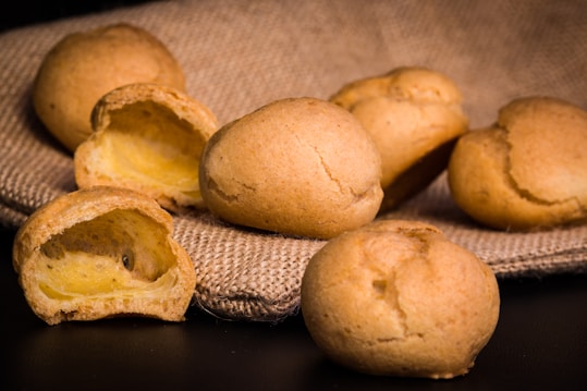 Golden-brown pastry puffs are arranged on a textured burlap cloth. The pastries appear fresh with a slightly crisp exterior and reveal a soft, creamy interior on the cut side.