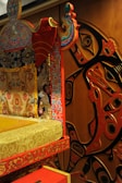 A richly decorated piece of furniture with intricate patterns and vibrant colors is placed next to a wall with abstract art. The furniture features floral and ornate designs in red, blue, and gold, while the wall art includes stylized, curved shapes in black and red.