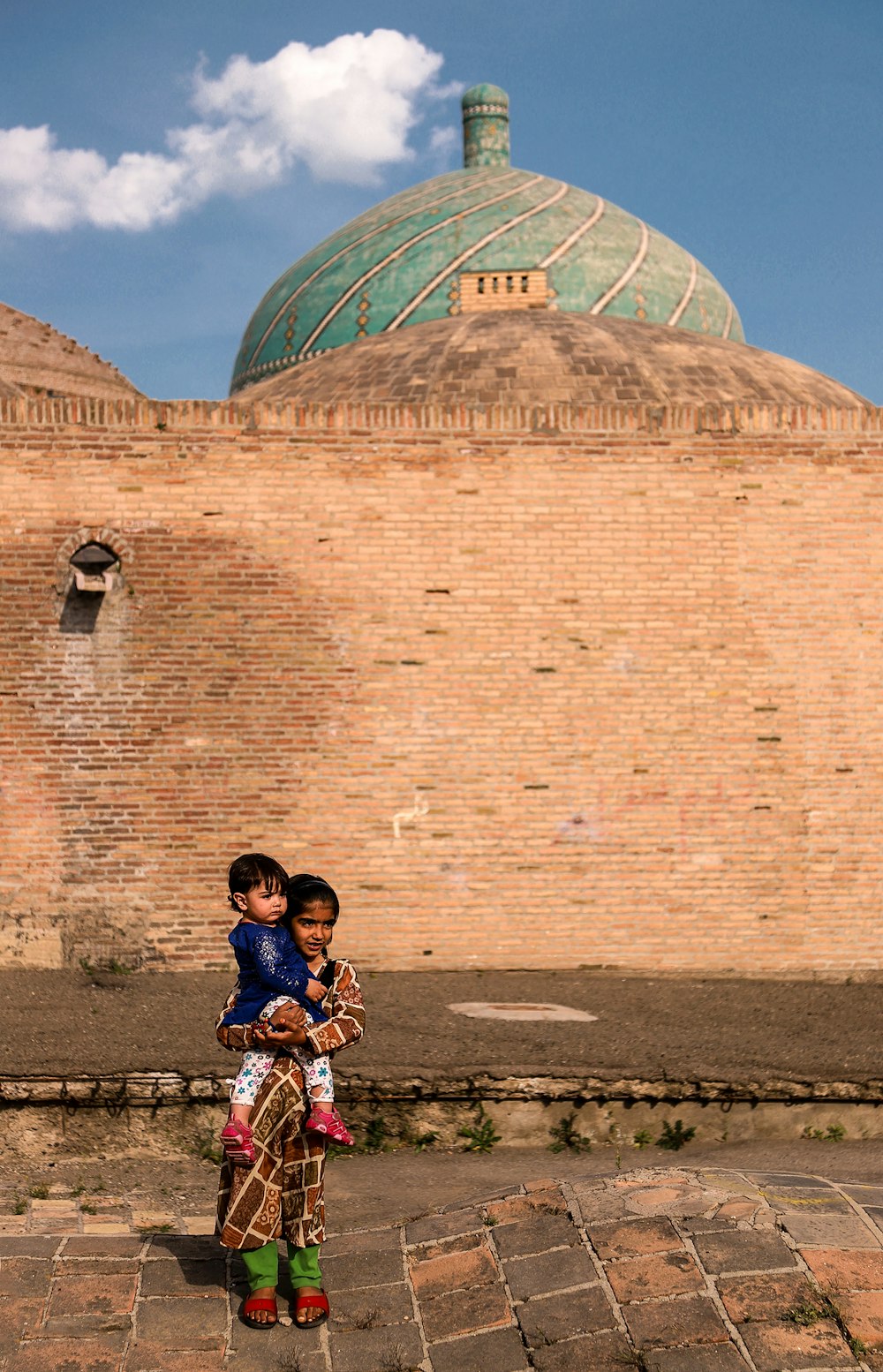 Muchacha que lleva a un niño pequeño de pie junto al edificio de la cúpula marrón y verde