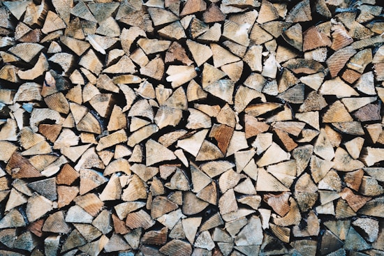 A large pile of chopped firewood pieces, neatly stacked and closely packed together. The wood displays various shades of brown, beige, and tan, highlighting the natural textures and grain patterns.