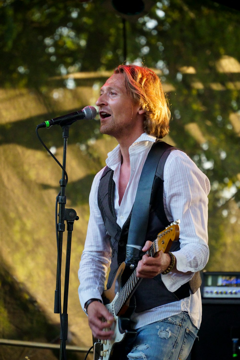 man holding black and white guitar standing beside black microphone close-up photography