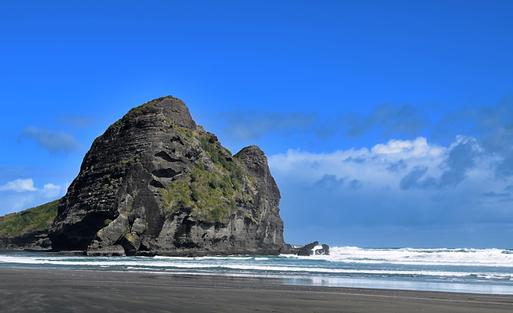 black and green rock formation beside body of water at daytime