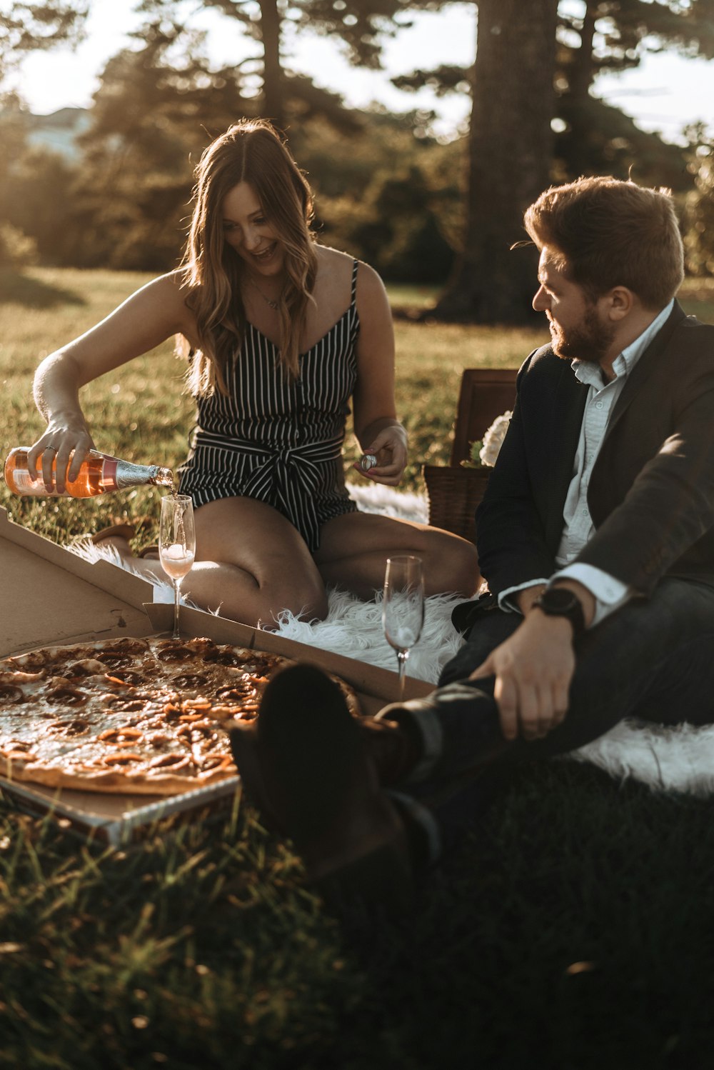 a man and a woman sitting on the grass eating pizza