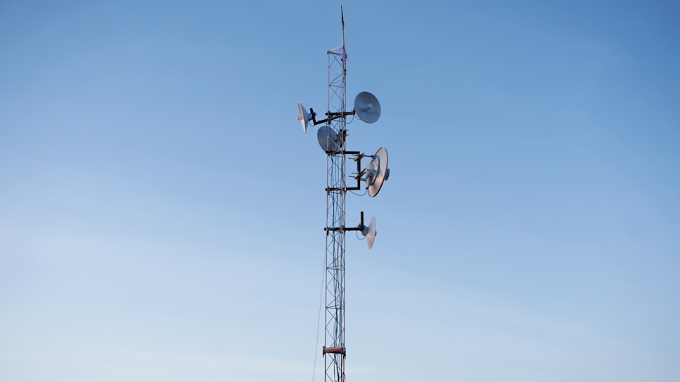 A tall communication tower with multiple Ubiquiti antennas against a clear blue sky.