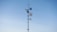 A tall communication tower is equipped with multiple satellite dishes and antennas against a clear blue sky.