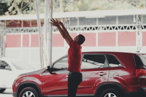 A happy customer shaking hands with a friendly car dealer near a red SUV.