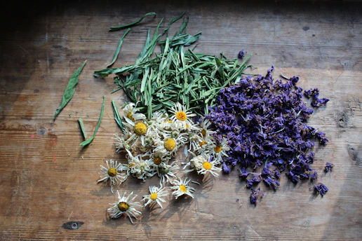 Loose dried chamomile flowers, lavender buds, and herb leaves spread on a rustic wood table for herb
