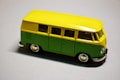 A miniature model of a van with a bright yellow roof and upper body, and a green lower body. The van features detailed wheels and windows, and reflects light on its smooth surface, creating a shiny appearance.