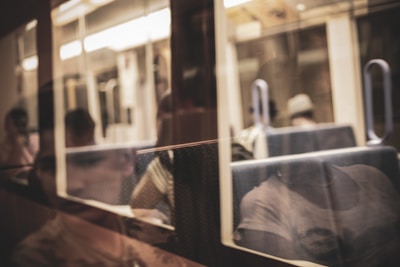 A reflection on a glass showing people sitting inside a dimly lit train carriage, with some parts appearing blurred. The focus seems to be on the reflections with a warm color tone.