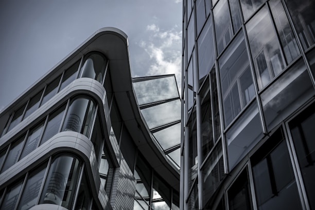 Modern architecture featuring two large glass and steel buildings with sleek, curved designs under a cloudy sky.