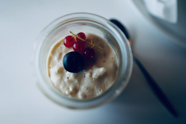 Close-up of a creamy dessert in a glass jar topped with fresh berries and mint leaves.