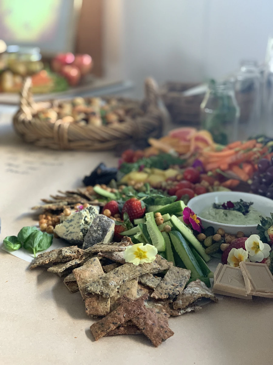 A vegetarian board of sliced cucumber, thin seeded crackers, berries, a bowl of dip and edible flowers