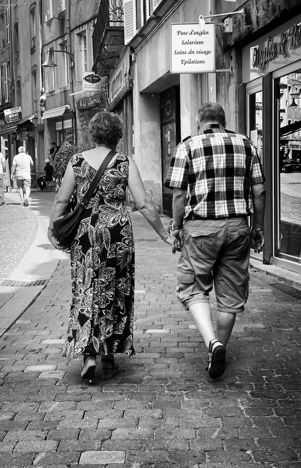 couple holding hands while walking on sidewalk