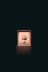 A single ring with a circular gemstone is elegantly displayed in an illuminated jewelry box set against a dark background. Soft lighting enhances the ring's sparkle and creates a luxurious atmosphere.
