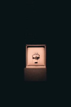 A single ring with a circular gemstone is elegantly displayed in an illuminated jewelry box set against a dark background. Soft lighting enhances the ring's sparkle and creates a luxurious atmosphere.