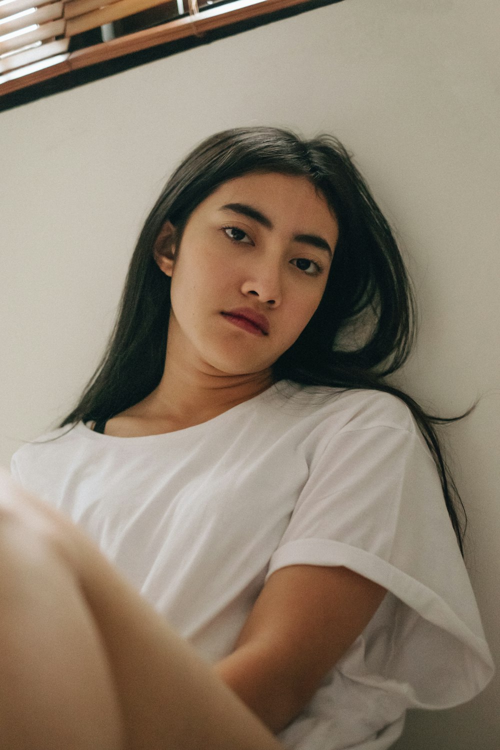 woman wearing white crew-neck t-shirt sitting and leaning against white wall