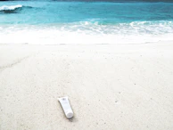 Close-up of hands holding a bottle of sunscreen with a backdrop of sunlit waves and sand.