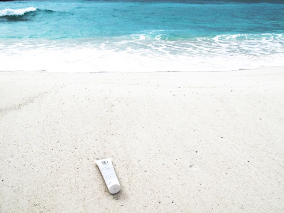 Bright blue and yellow sun cream tube on a sandy beach with ocean waves in the background