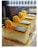 Three beautifully decorated slices of cake are displayed in a well-lit setting. Each slice has a smooth, creamy texture and is topped with a layer of orange glaze, a single macaron, and a small piece of dark chocolate. The cakes rest on golden bases, emphasizing a luxurious presentation.