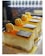 Three beautifully decorated slices of cake are displayed in a well-lit setting. Each slice has a smooth, creamy texture and is topped with a layer of orange glaze, a single macaron, and a small piece of dark chocolate. The cakes rest on golden bases, emphasizing a luxurious presentation.
