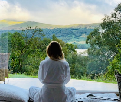 sitting woman in white robe looking at mountains during daytime tranquil zoom background