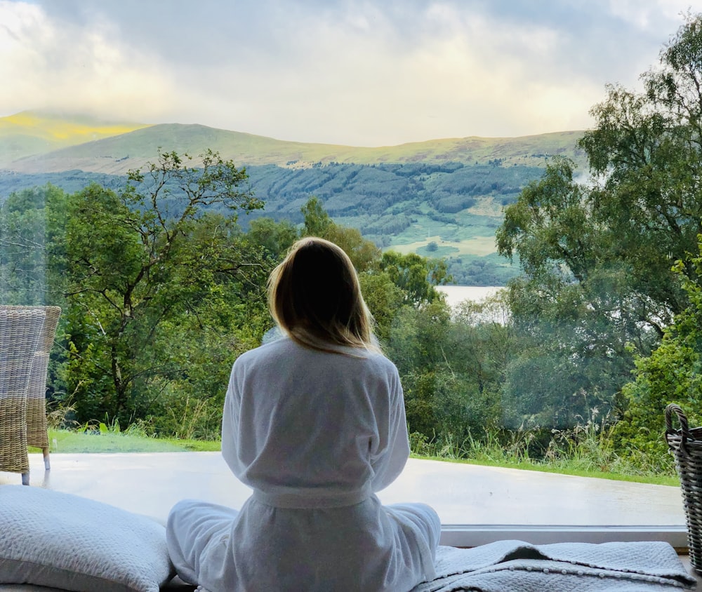 mulher sentada no manto branco olhando para as montanhas durante o dia