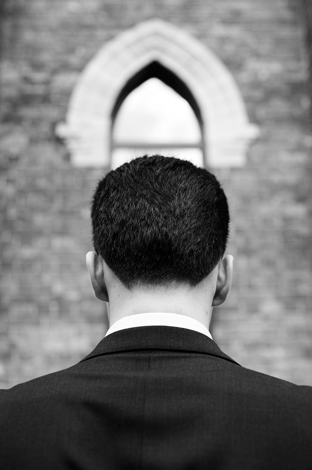grayscale photography of man facing back near wall
